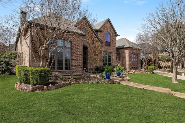 view of front facade with a front lawn, brick siding, stone siding, and a chimney