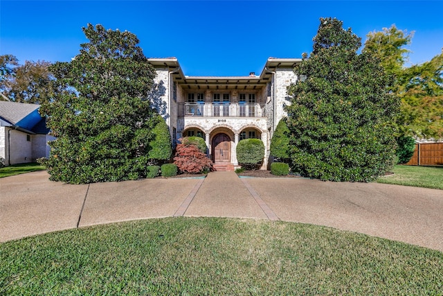 view of front of house featuring a front yard, stone siding, and a balcony