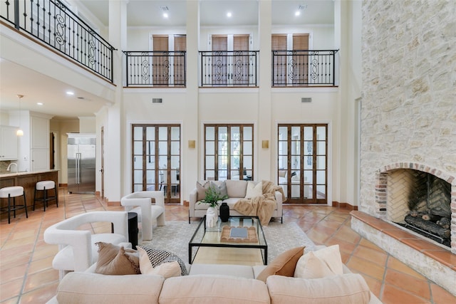 living room featuring light tile patterned floors, a stone fireplace, a high ceiling, visible vents, and crown molding