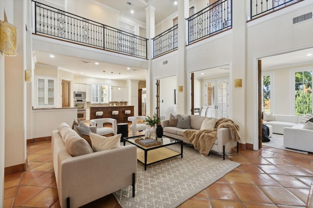 tiled living area with decorative columns, visible vents, baseboards, a towering ceiling, and ornamental molding