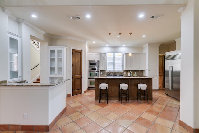 kitchen featuring a breakfast bar, visible vents, decorative backsplash, white cabinets, and built in appliances