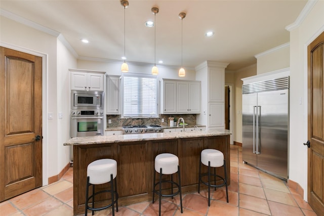 kitchen with an island with sink, built in appliances, light stone countertops, crown molding, and backsplash