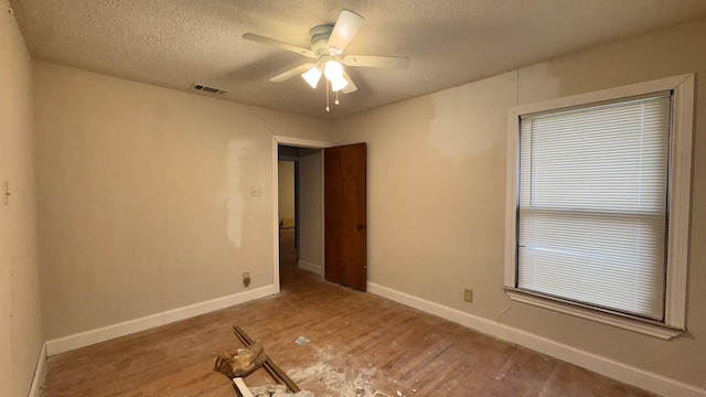 unfurnished room with baseboards, visible vents, ceiling fan, wood finished floors, and a textured ceiling