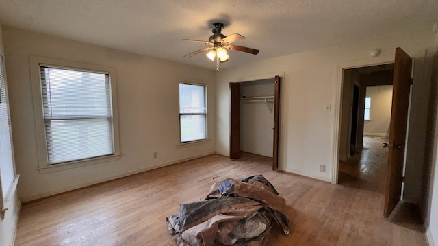 unfurnished bedroom with light wood-style floors, ceiling fan, baseboards, and a closet