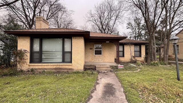 view of front of house featuring a front yard, a chimney, and brick siding