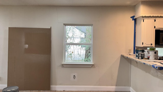 kitchen featuring light countertops, black microwave, white cabinets, and baseboards