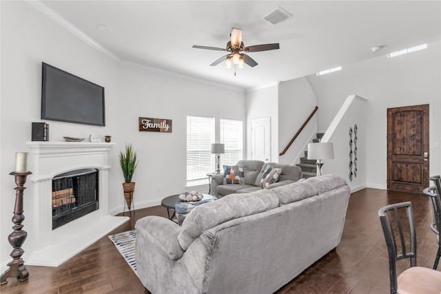 living room with a fireplace with raised hearth, visible vents, stairway, dark wood-style floors, and crown molding