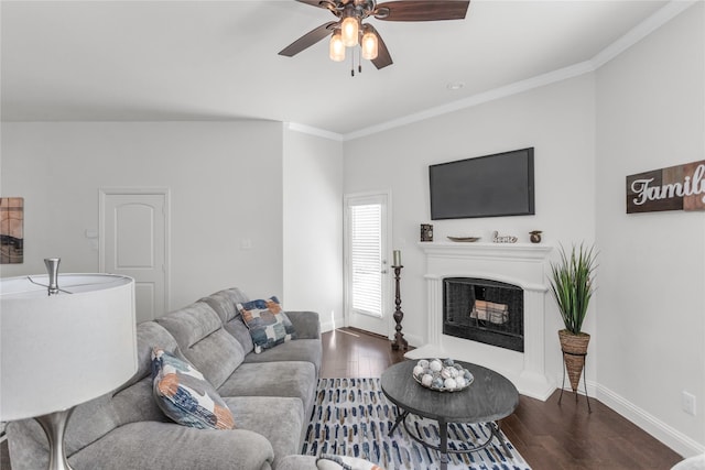 living area featuring baseboards, a fireplace with raised hearth, ceiling fan, wood finished floors, and crown molding