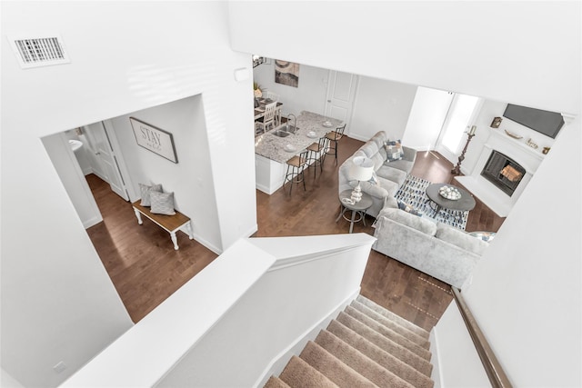 staircase featuring a fireplace with flush hearth, wood finished floors, and visible vents