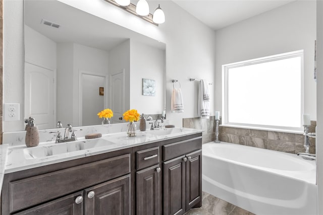 bathroom featuring a bath, double vanity, a sink, and visible vents