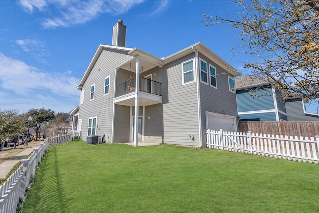 back of property with a lawn, an attached garage, central AC, a balcony, and a fenced backyard