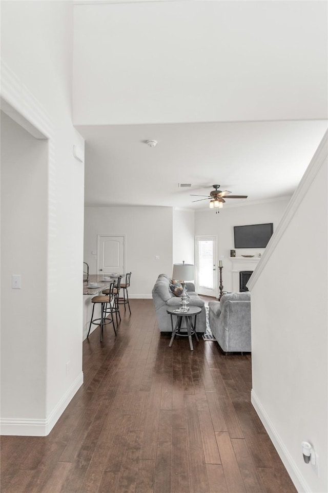 living area featuring dark wood-style floors, ceiling fan, a fireplace, and baseboards