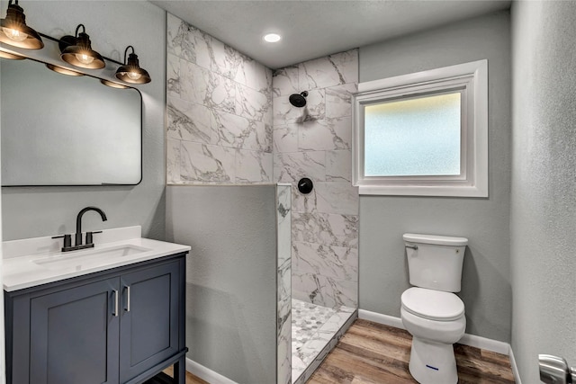 bathroom with baseboards, toilet, wood finished floors, a tile shower, and vanity