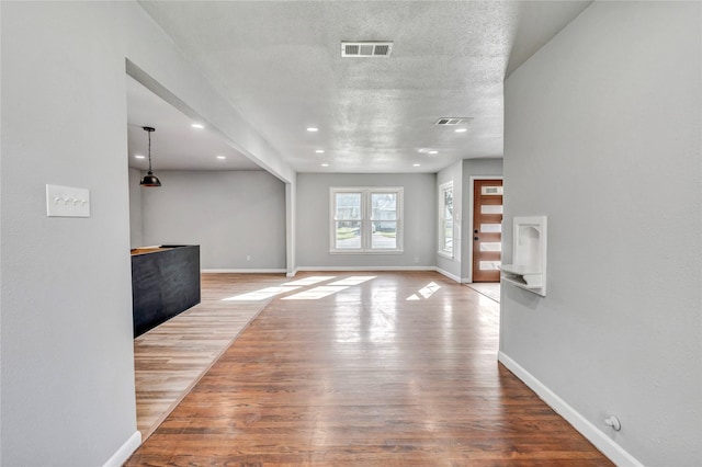 unfurnished living room featuring visible vents, a textured ceiling, baseboards, and wood finished floors