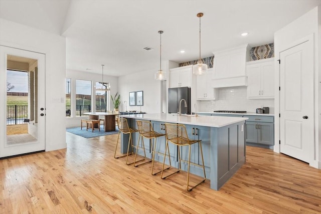 kitchen featuring tasteful backsplash, a breakfast bar area, stainless steel refrigerator, a kitchen island with sink, and light countertops