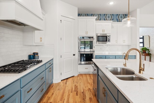 kitchen featuring custom range hood, hanging light fixtures, appliances with stainless steel finishes, white cabinets, and a sink