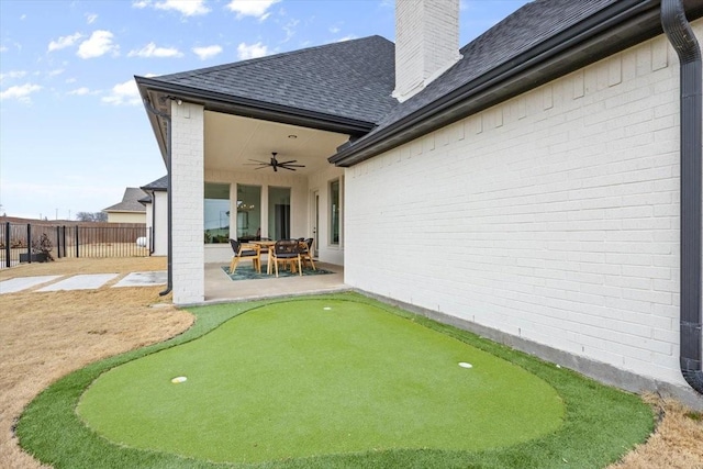 back of property featuring a patio, ceiling fan, a chimney, roof with shingles, and fence