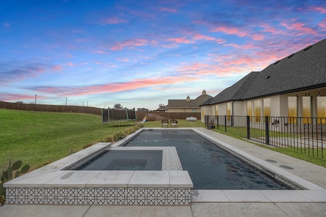 pool at dusk featuring an in ground hot tub, a fenced backyard, a trampoline, and a yard