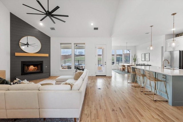 living room featuring high vaulted ceiling, a large fireplace, visible vents, a ceiling fan, and light wood finished floors