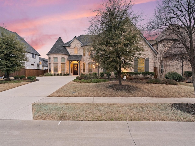 french country inspired facade featuring concrete driveway, stone siding, and fence