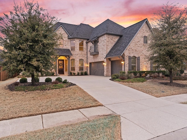 french provincial home featuring driveway, brick siding, and an attached garage