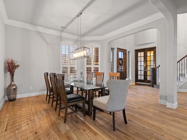 dining area with light wood finished floors, arched walkways, stairs, french doors, and a notable chandelier