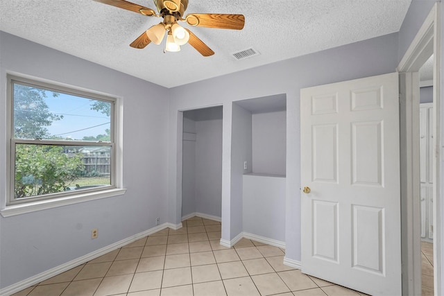 unfurnished bedroom featuring light tile patterned floors, a ceiling fan, visible vents, baseboards, and a textured ceiling