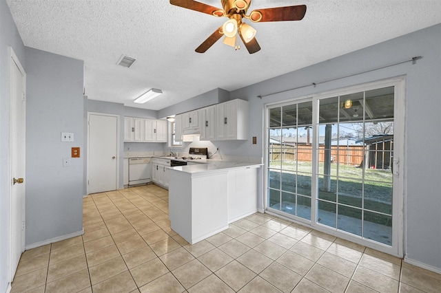 kitchen featuring range with gas stovetop, a peninsula, white dishwasher, light countertops, and white cabinetry