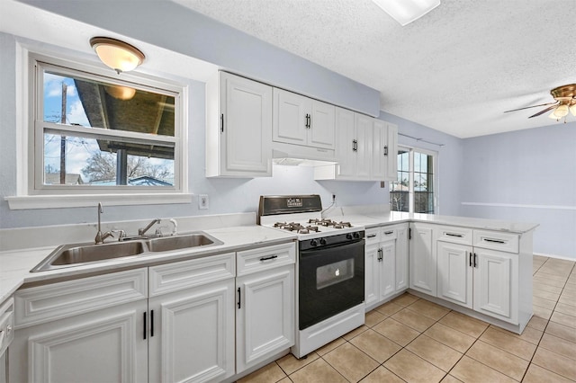 kitchen with under cabinet range hood, a peninsula, white cabinets, gas stove, and a sink