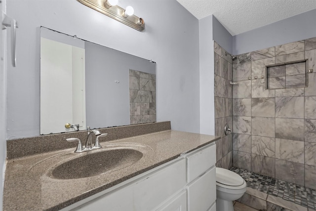 bathroom with a tile shower, a textured ceiling, toilet, and vanity