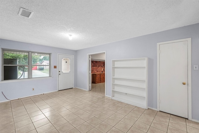 unfurnished room featuring light tile patterned floors, visible vents, built in shelves, and a textured ceiling