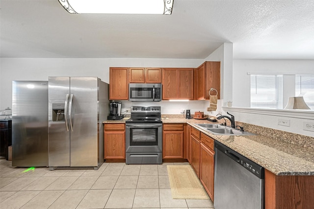 kitchen featuring light tile patterned floors, appliances with stainless steel finishes, brown cabinetry, and a sink