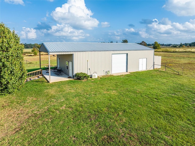 view of pole building with driveway, a rural view, fence, and a yard