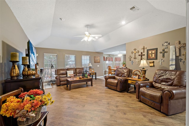 living area featuring a tray ceiling, visible vents, light wood-style flooring, vaulted ceiling, and ceiling fan