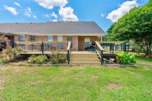 back of property with brick siding, roof with shingles, a lawn, and a wooden deck