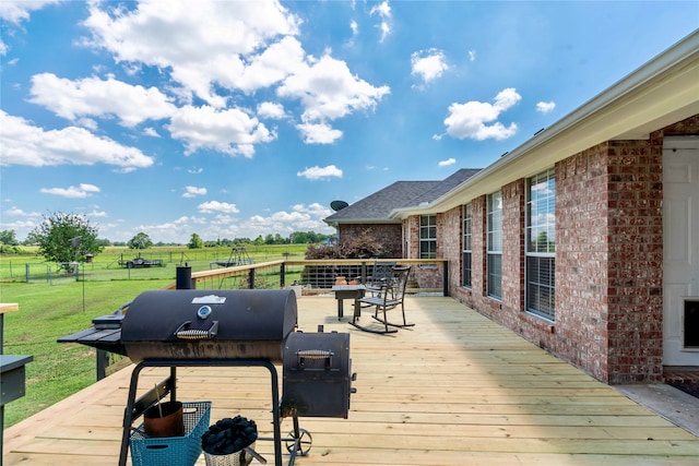 wooden deck featuring a rural view, fence, grilling area, and a lawn