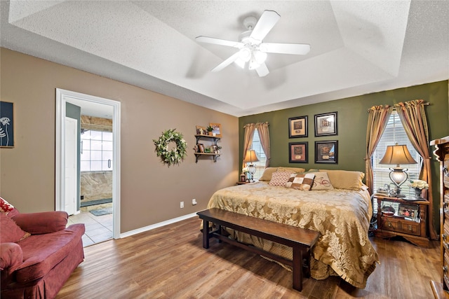 bedroom with a tray ceiling, a textured ceiling, baseboards, and wood finished floors