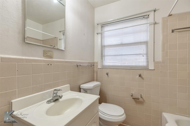 bathroom with wainscoting, toilet,  shower combination, vanity, and tile walls