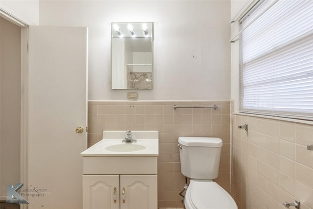 bathroom featuring toilet, vanity, tile walls, and wainscoting