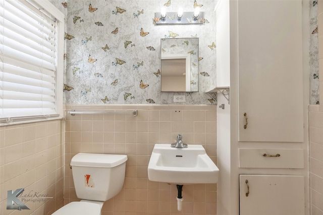 half bathroom with wainscoting, a sink, toilet, and wallpapered walls