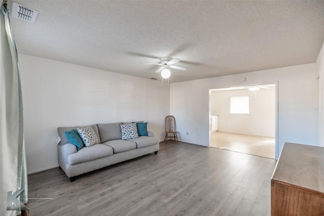 living room featuring a ceiling fan, a textured ceiling, visible vents, and wood finished floors