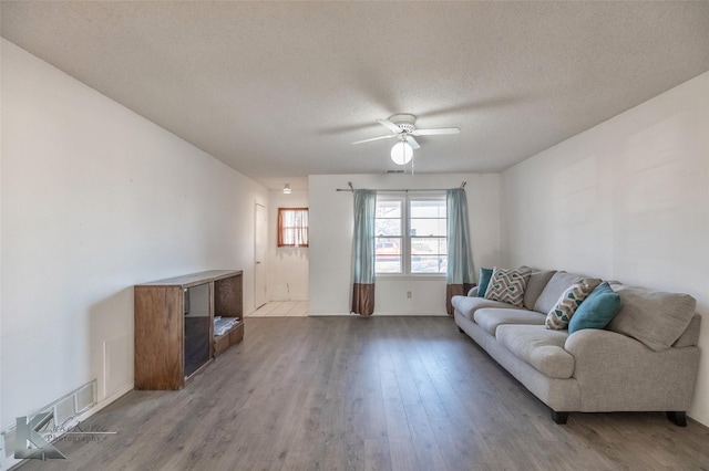 living room with a textured ceiling, visible vents, wood finished floors, and a ceiling fan