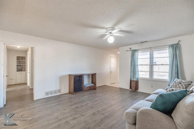 living room with a ceiling fan, a textured ceiling, visible vents, and wood finished floors