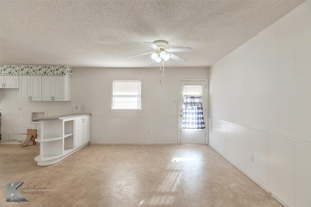 empty room featuring a textured ceiling, light floors, wainscoting, and a ceiling fan