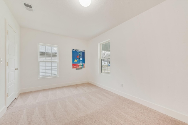 spare room featuring baseboards, plenty of natural light, visible vents, and light colored carpet