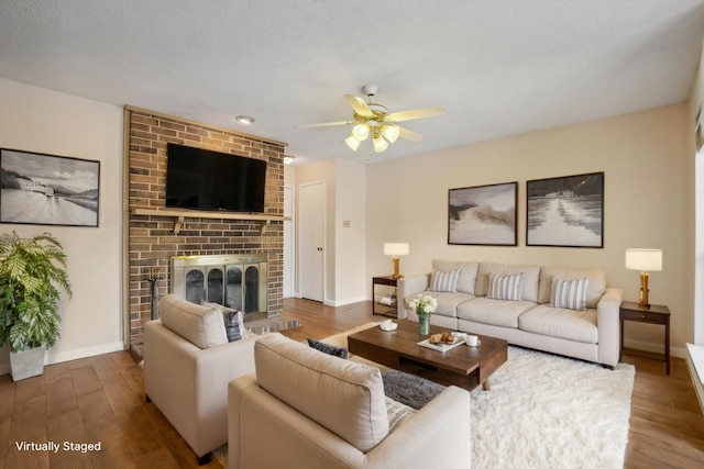 living area featuring a brick fireplace, wood finished floors, a ceiling fan, and baseboards