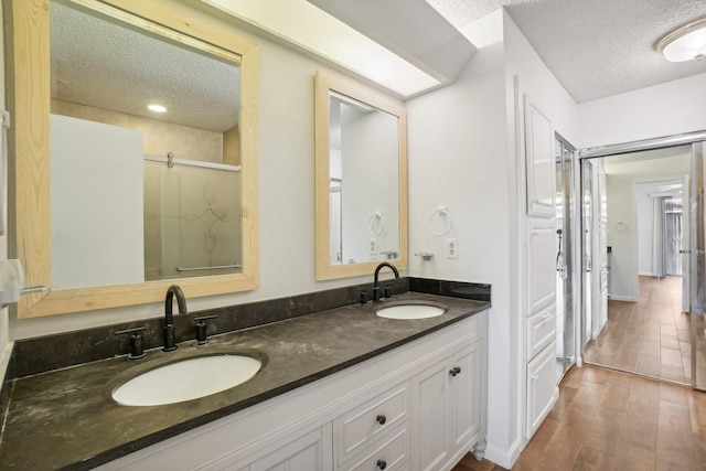 full bathroom with a sink, a shower stall, a textured ceiling, and wood finished floors