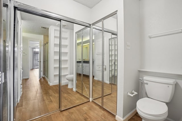 bathroom with toilet, a textured ceiling, visible vents, and wood finished floors