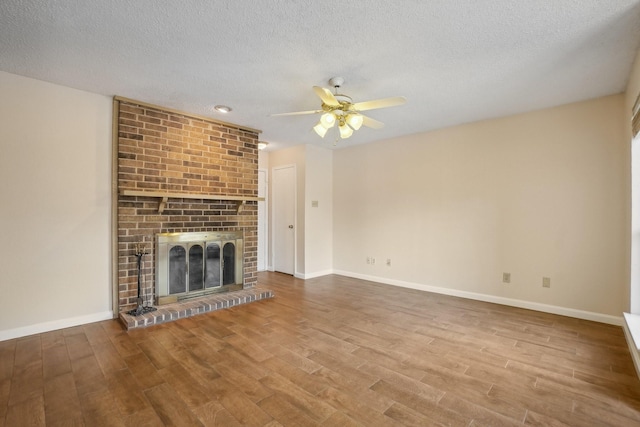 unfurnished living room with a brick fireplace, a textured ceiling, baseboards, and wood finished floors