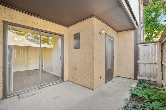 view of exterior entry featuring a patio area, fence, and stucco siding